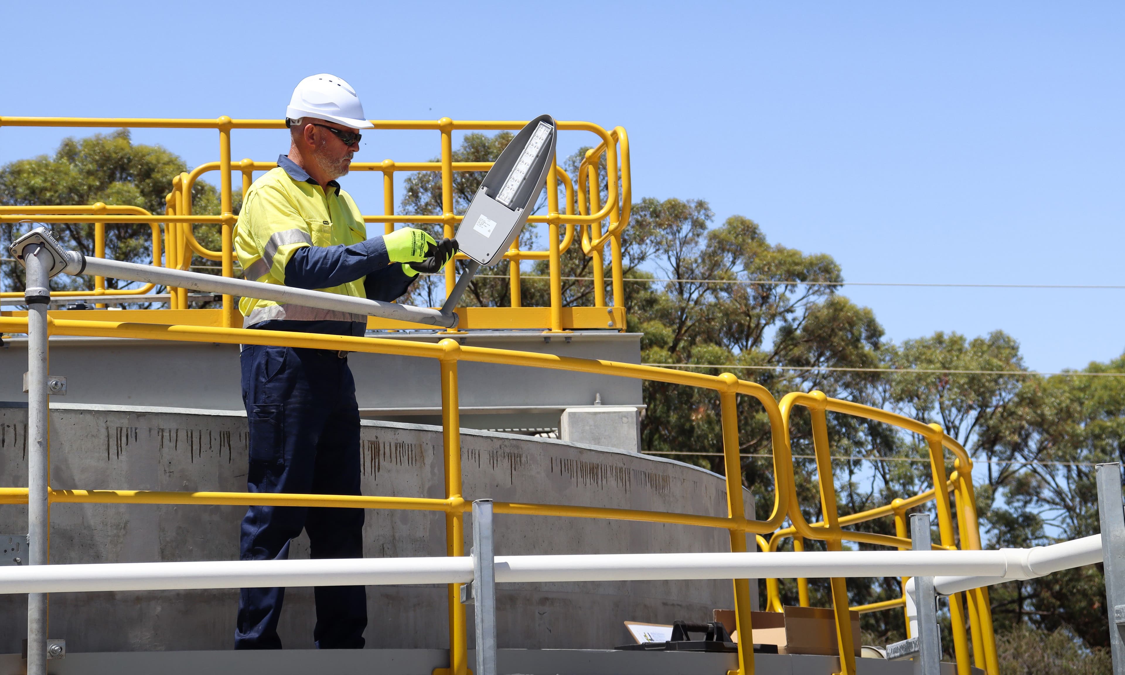Worker safely accessing a light fixture using a Swivelpole lowering pole at a water treatment plant